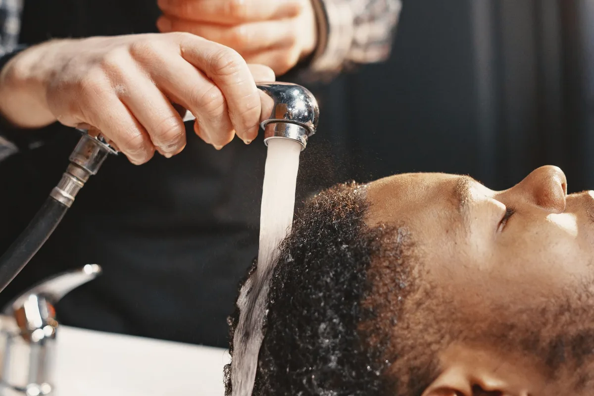 Mains massant doucement le cuir chevelu de cheveux bouclés mouillés pendant un soin de réinitialisation