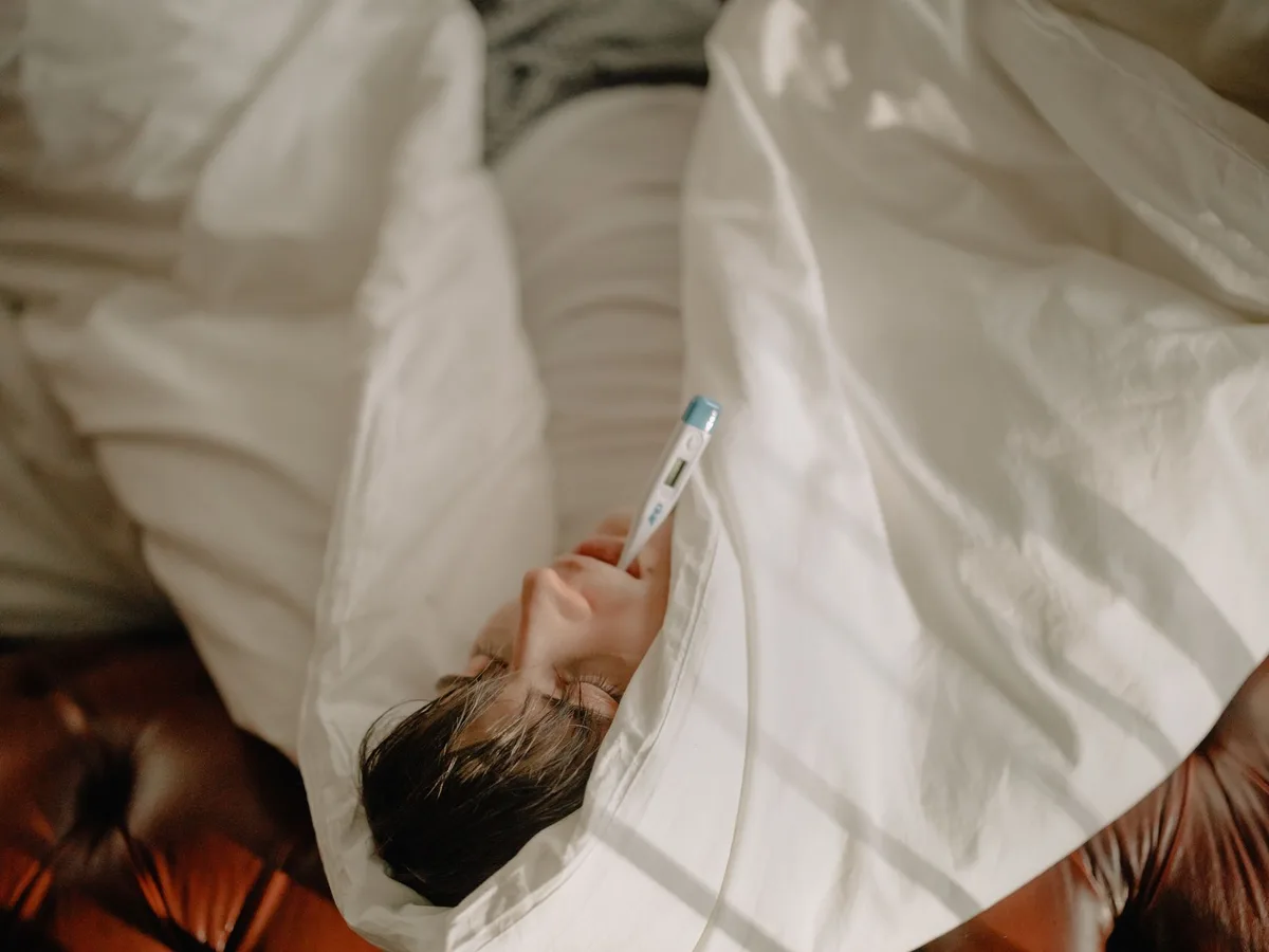 Personne au repos au lit avec une boisson chaude pour soulager les symptômes de la grippe