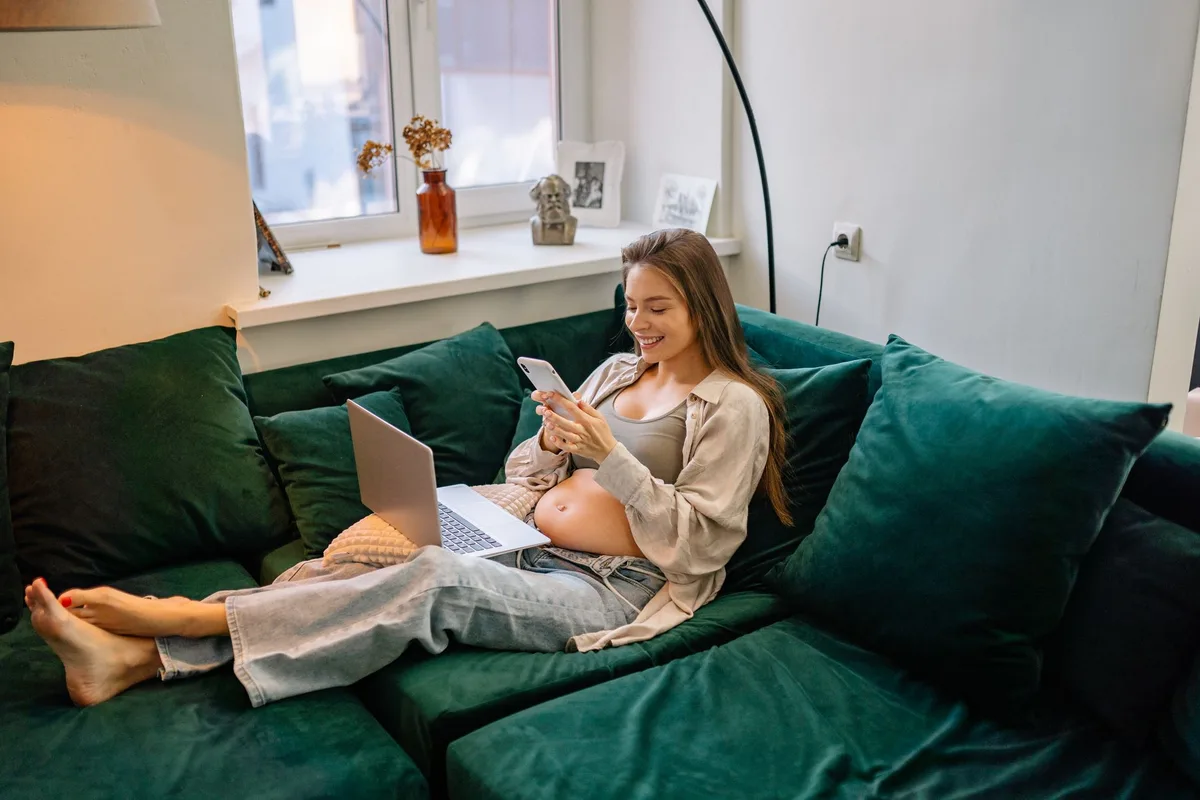 Femme enceinte se reposant sur un canapé avec une couverture, verre d'eau et fruits à proximité