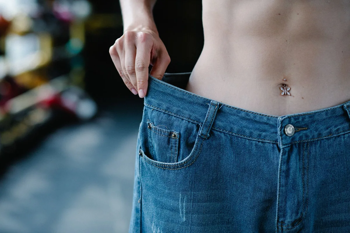 Personne pesant sur une balance de salle de bain avec des aliments et un journal de fitness à proximité