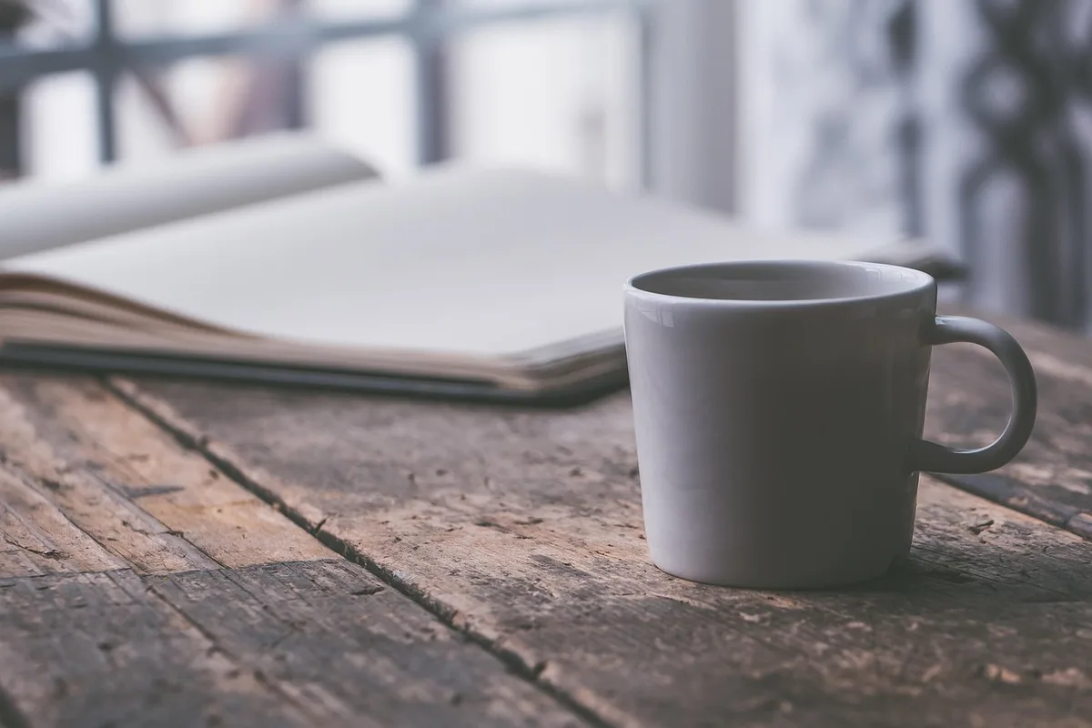 Parent prenant une micro‑pause avec une tasse près d'une fenêtre lumineuse