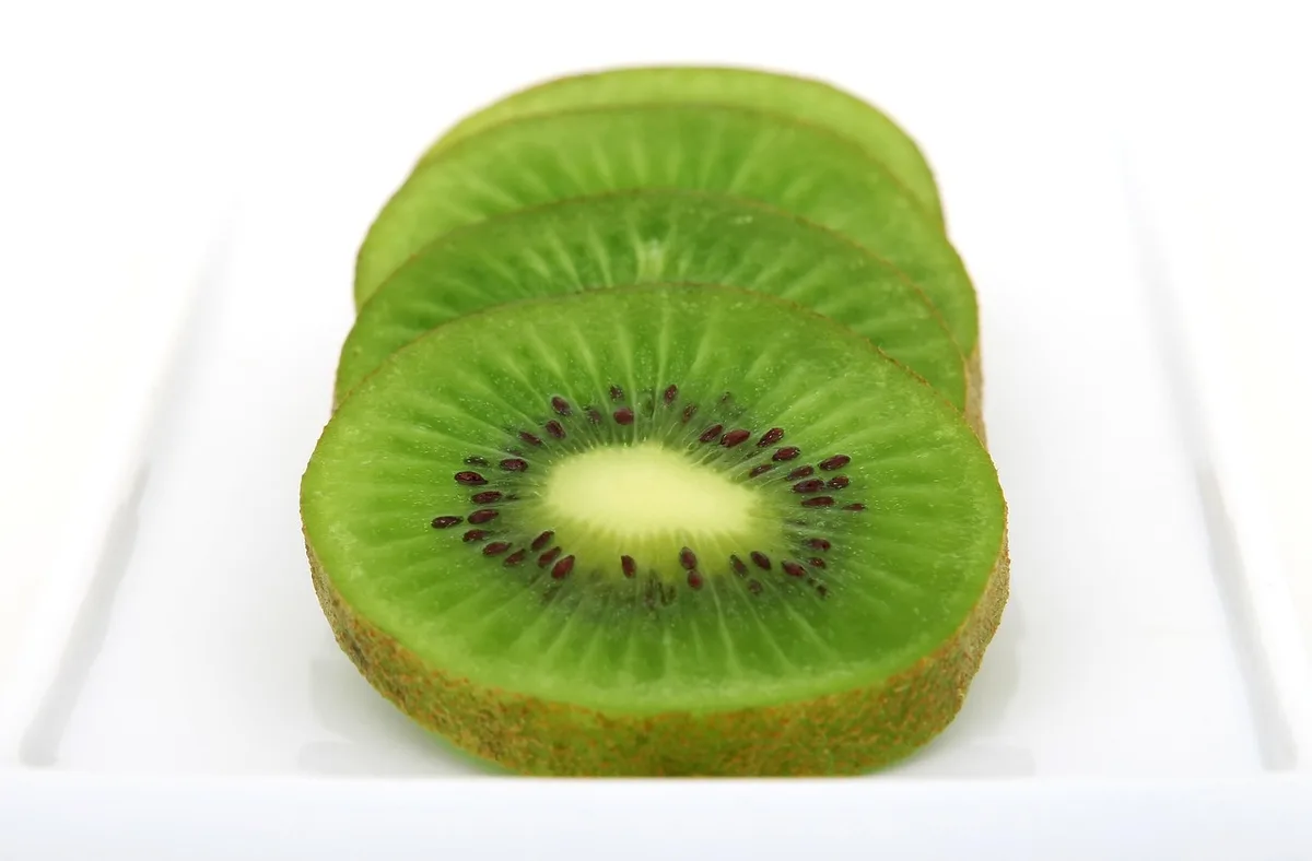 Mains anonymes coupant un kiwi mûr sur une table de cuisine en plein jour