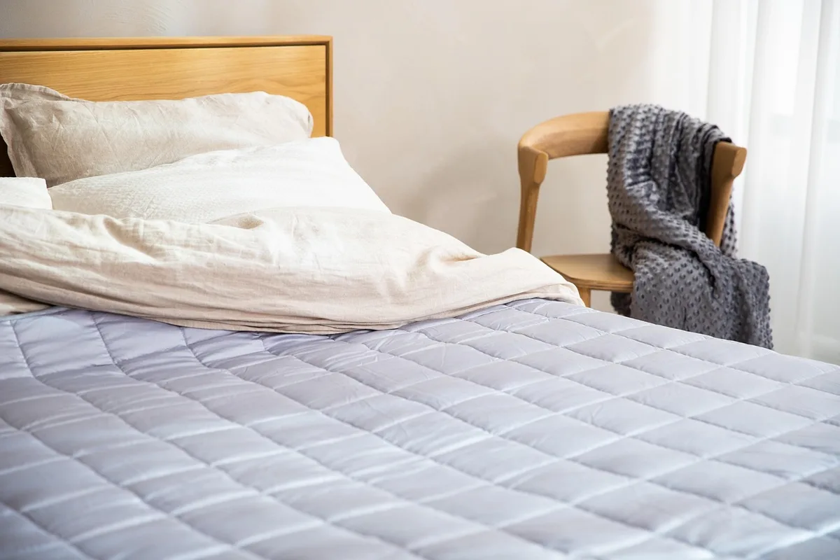 Chambre en pleine journée avec couette en coton rabattue et thermomètre sur la table de chevet